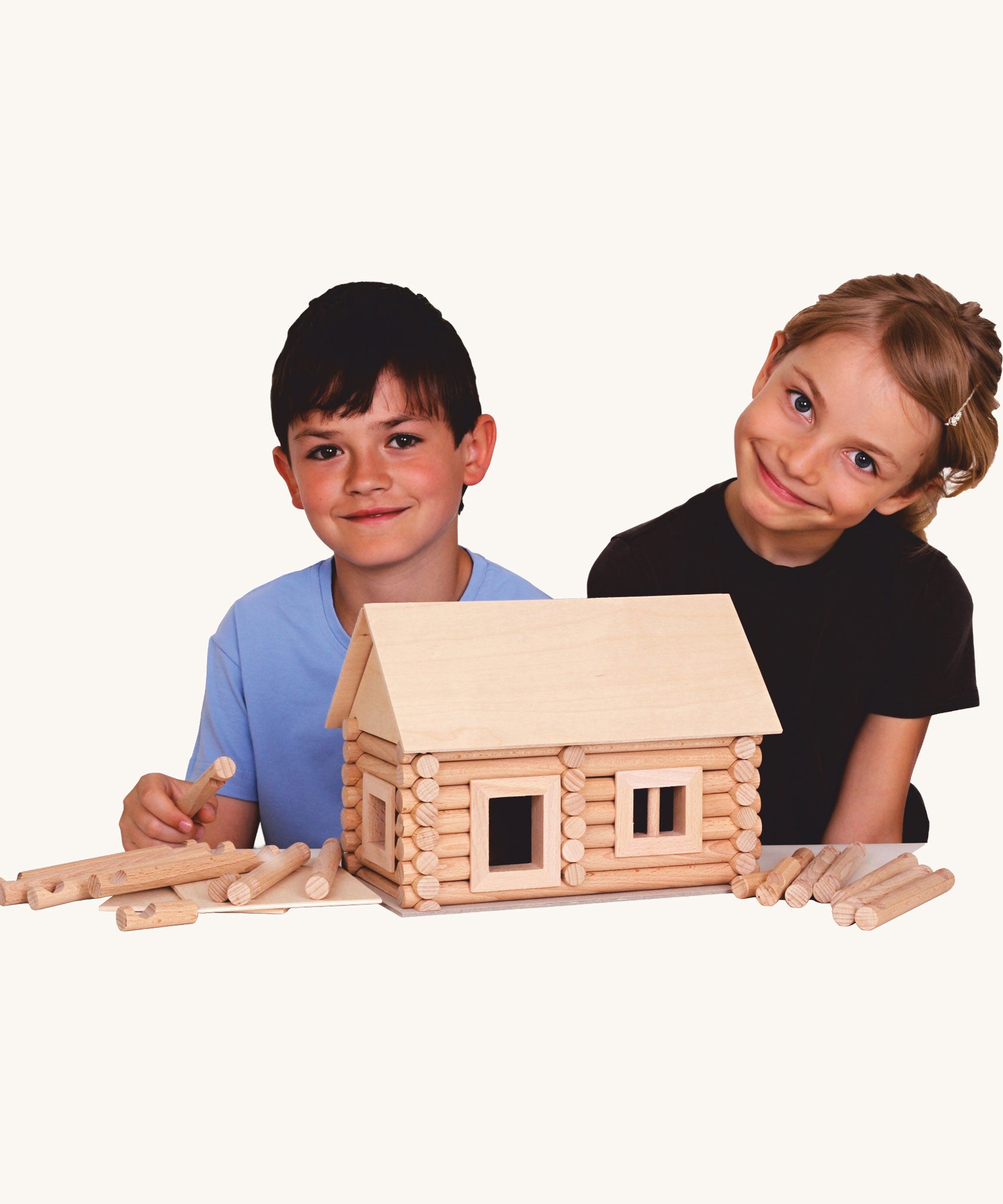 Two children smiling with a log cabin created using wooden blocks from the Walachia Vario Building Sets in front of them. This modular wooden building block system is perfect for those who enjoy a challenge. The sets are available in various sizes at Babipur.  