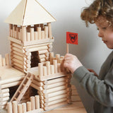 A child putting the flag pole in place on a fort build created using the Walachia Vario Fort Building Set 194 Pieces. This modular wooden building block system is perfect for those who enjoy a challenge. The sets are available in various sizes at Babipur. 