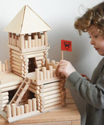 A child putting the flag pole in place on a fort build created using the Walachia Vario Fort Building Set 194 Pieces. This modular wooden building block system is perfect for those who enjoy a challenge. The sets are available in various sizes at Babipur. 