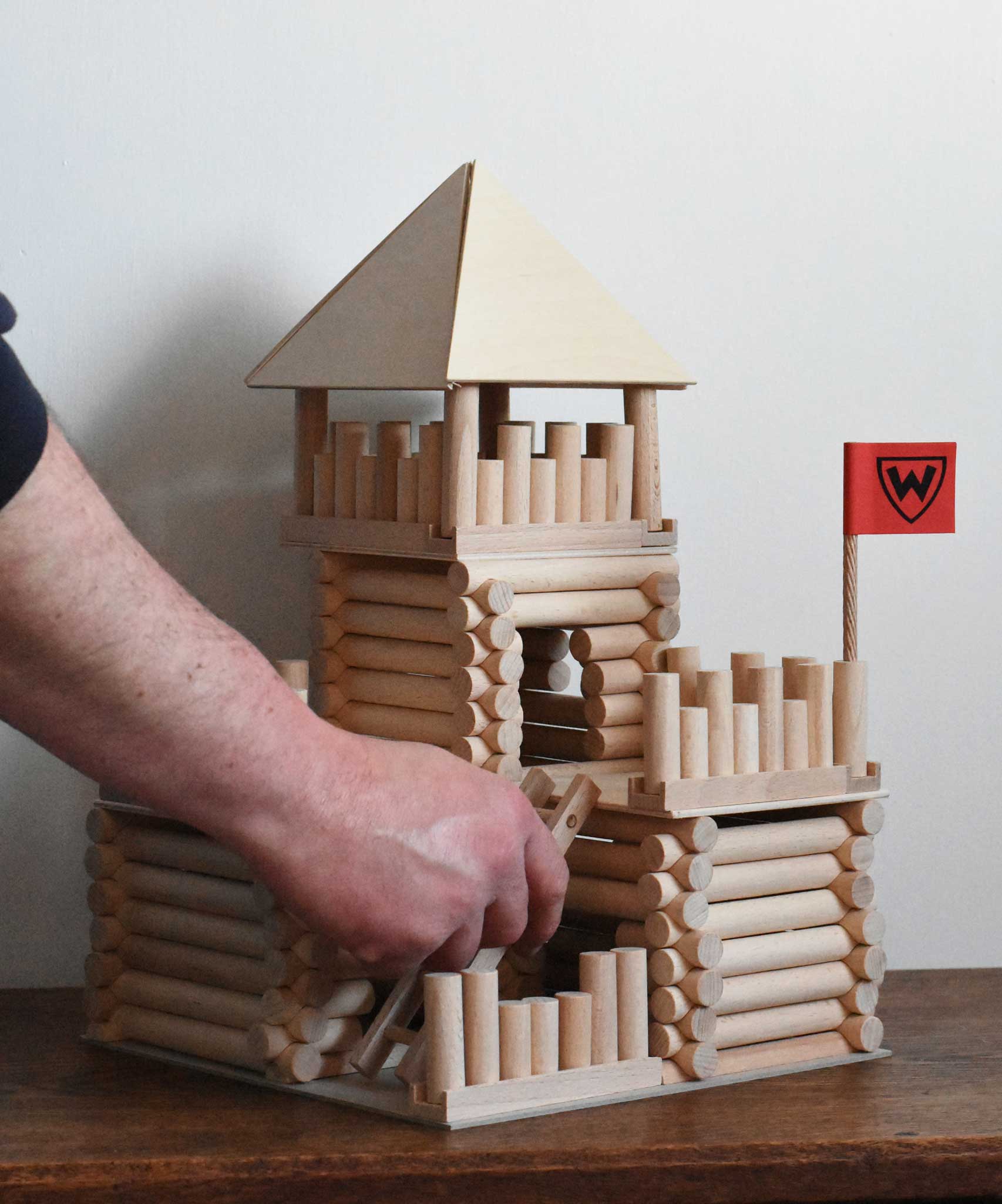 The ladder piece being placed on a fort build created using the Walachia Vario Fort Building Set 194 Pieces. This modular wooden building block system is perfect for those who enjoy a challenge. The sets are available in various sizes at Babipur. 