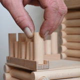 A close up of an adult's hand placing one of the blocks on a base piece to create a fence as part of a fort build created using the Walachia Vario Fort Building Set 194 Pieces. This modular wooden building block system is perfect for those who enjoy a challenge. The sets are available in various sizes at Babipur. 