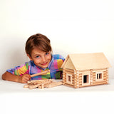 A child with a log cabin created using wooden blocks from the Walachia Vario Building Sets in front of them. This modular wooden building block system is perfect for those who enjoy a challenge. The sets are available in various sizes at Babipur.  