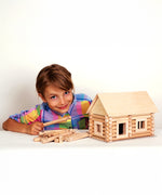 A child with a log cabin created using wooden blocks from the Walachia Vario Building Sets in front of them. This modular wooden building block system is perfect for those who enjoy a challenge. The sets are available in various sizes at Babipur.  