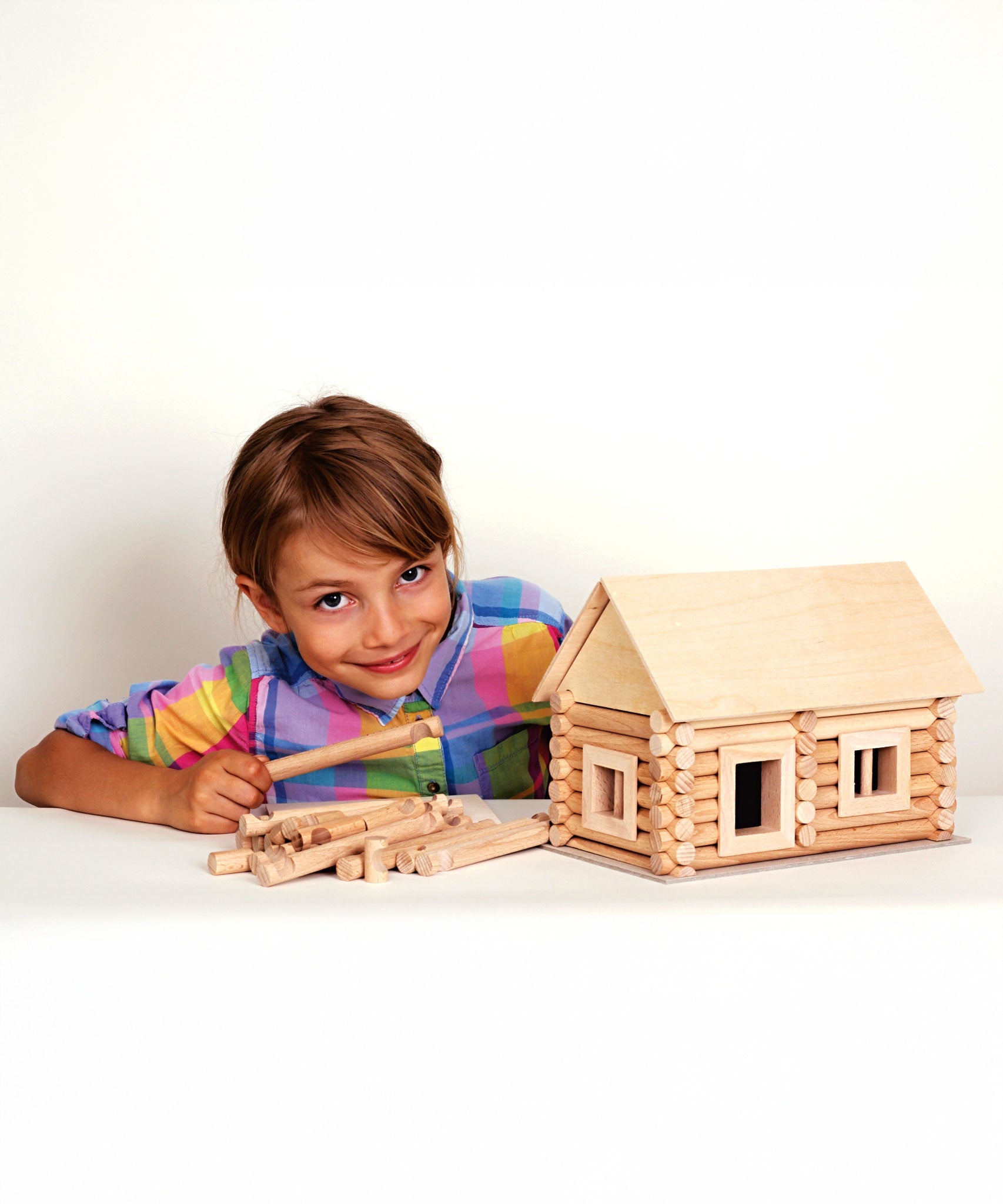 A child with a log cabin created using wooden blocks from the Walachia Vario Building Sets in front of them. This modular wooden building block system is perfect for those who enjoy a challenge. The sets are available in various sizes at Babipur.  