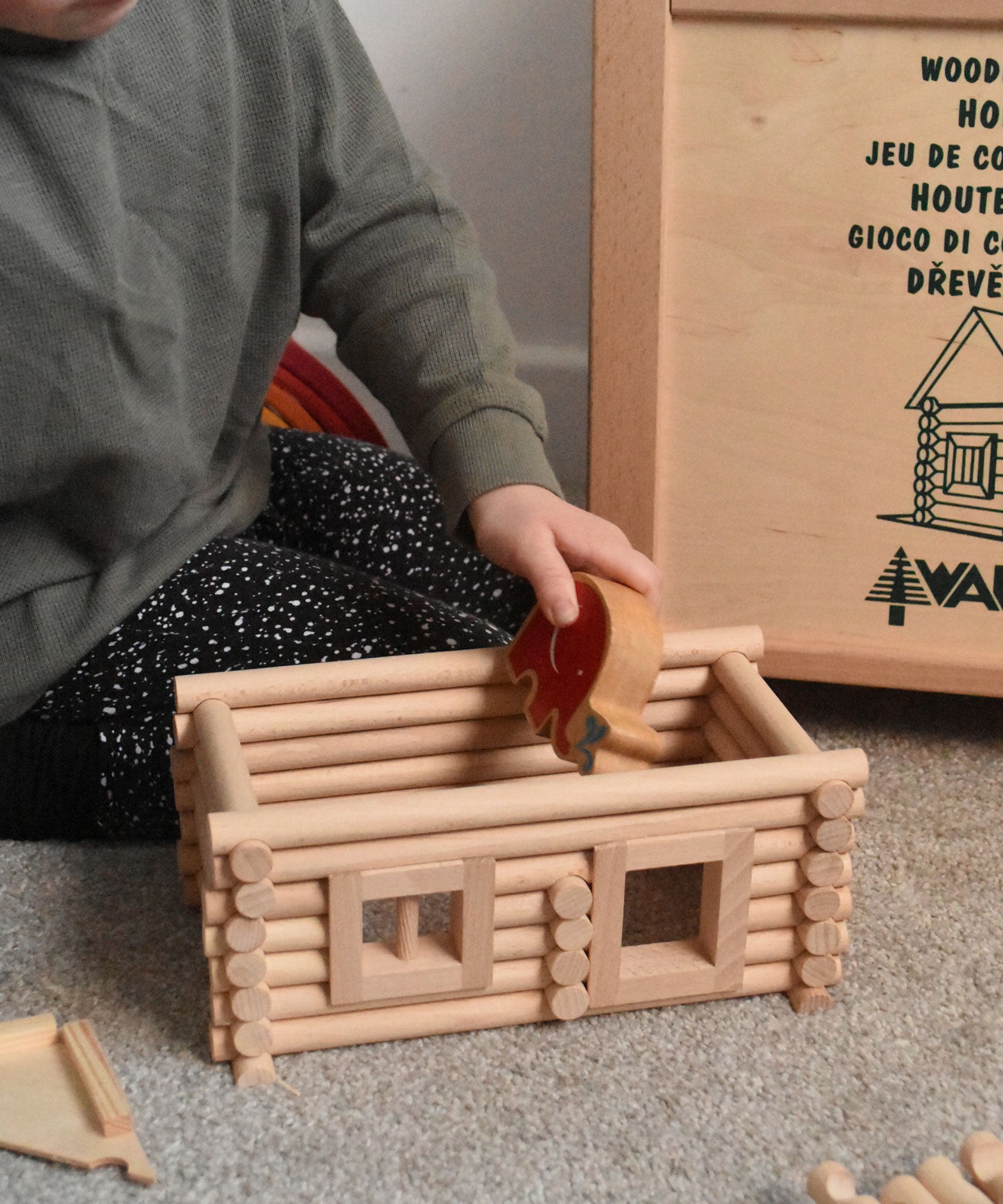 A child placing a Lanka Kade Babipur elephant figure inside a cabin created using wooden blocks from the Walachia Vario Building Sets. This modular wooden building block system is perfect for those who enjoy a challenge. The sets are available in various sizes at Babipur.  