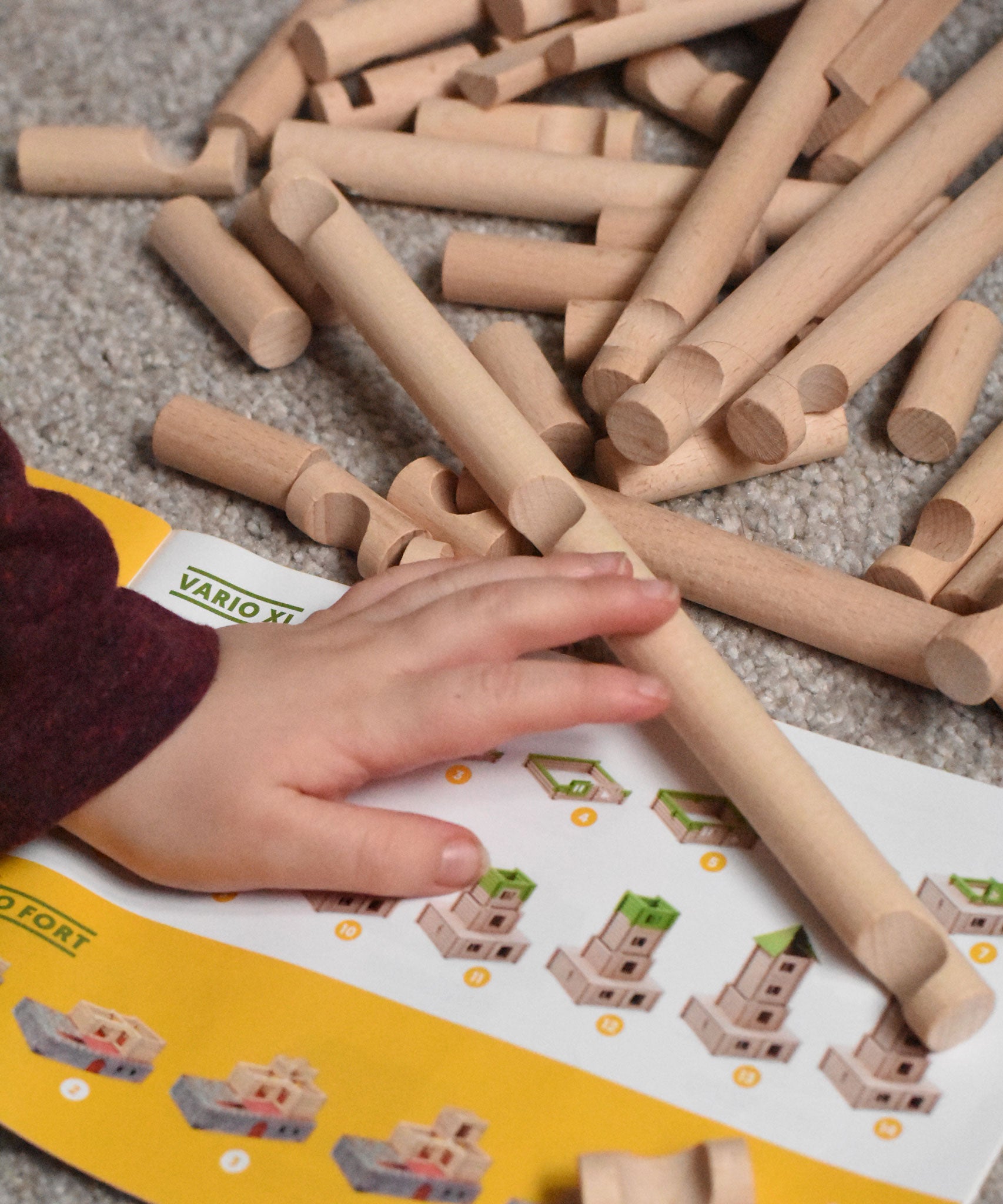 A child's hand reaching for Walachia Vario wooden log shaped blocks. This modular wooden building block system is perfect for those who enjoy a challenge. The sets are available in various sizes at Babipur.  