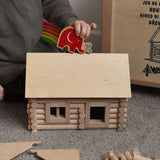 A child placing a Lanka Kade Babipur elephant figure on the roof of a cabin created using wooden blocks from the Walachia Vario Building Sets. This modular wooden building block system is perfect for those who enjoy a challenge. The sets are available in various sizes at Babipur.  