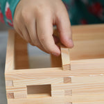 A close up of the wooden sticks being glued and put together to creating an amazing WALACHIA building. A child is carefully adding the wooden stick to the building