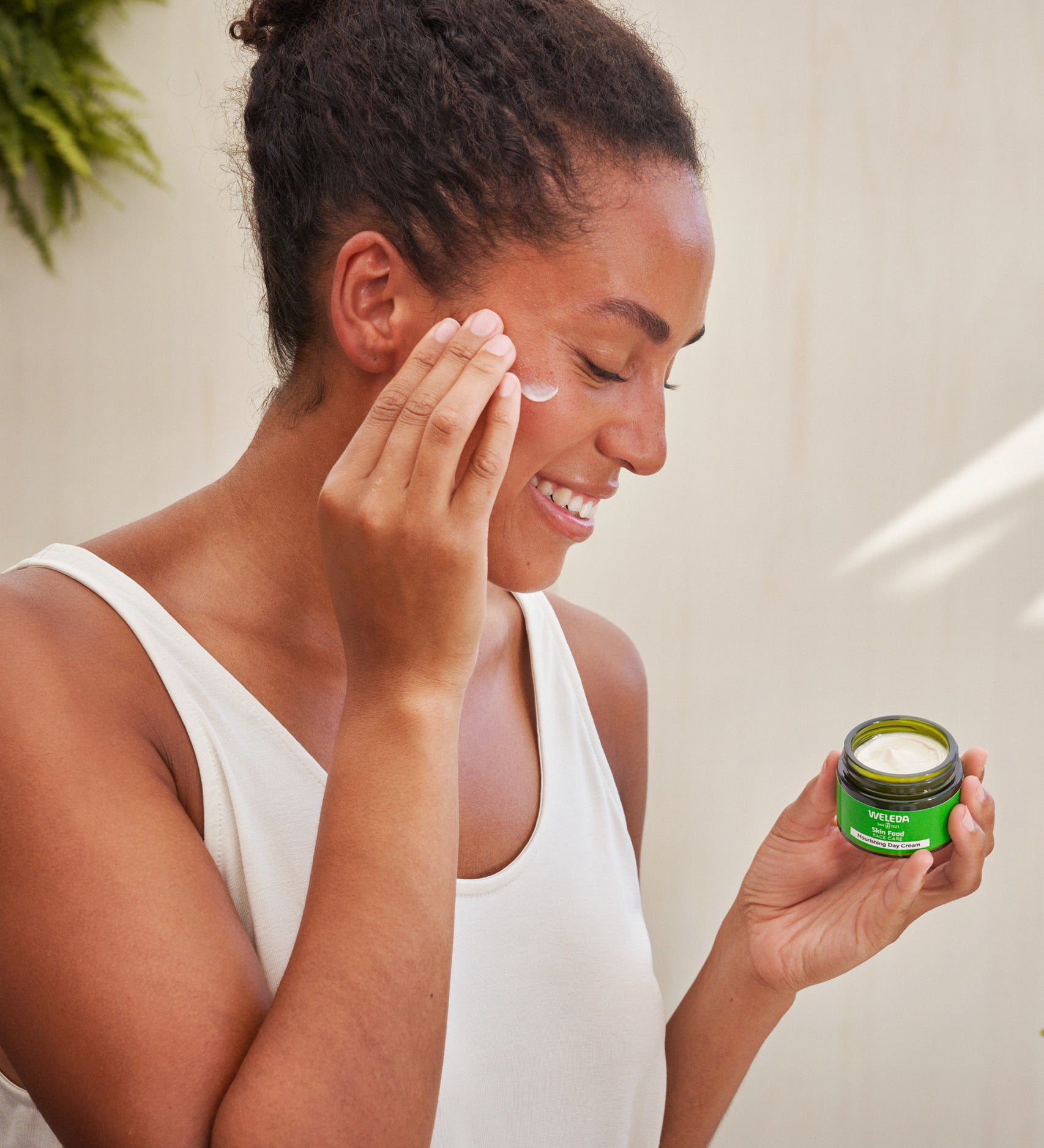 An image of a woman applying the Weleda Skin Food Nourishing Day Face Cream to their cheeks. This cream is available at Babipur.