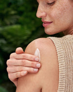 A close up shot of an adult smiling and using the Weleda Skin Foot set cream on their face