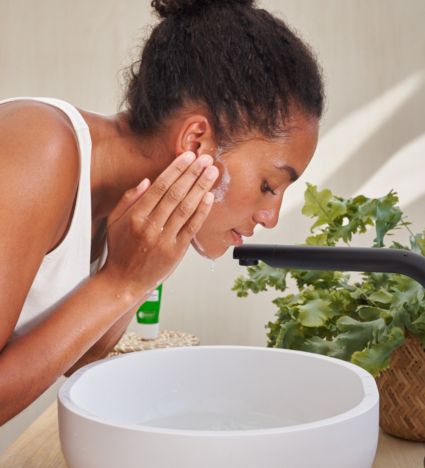 An image of a woman lathering the Weleda Skin Food nourishing cleansing balm above a sink . This cream is available at Babipur.