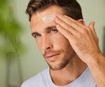 Man applying Weleda Men’s Organic Moisture Cream to his forehead in a bathroom setting.
