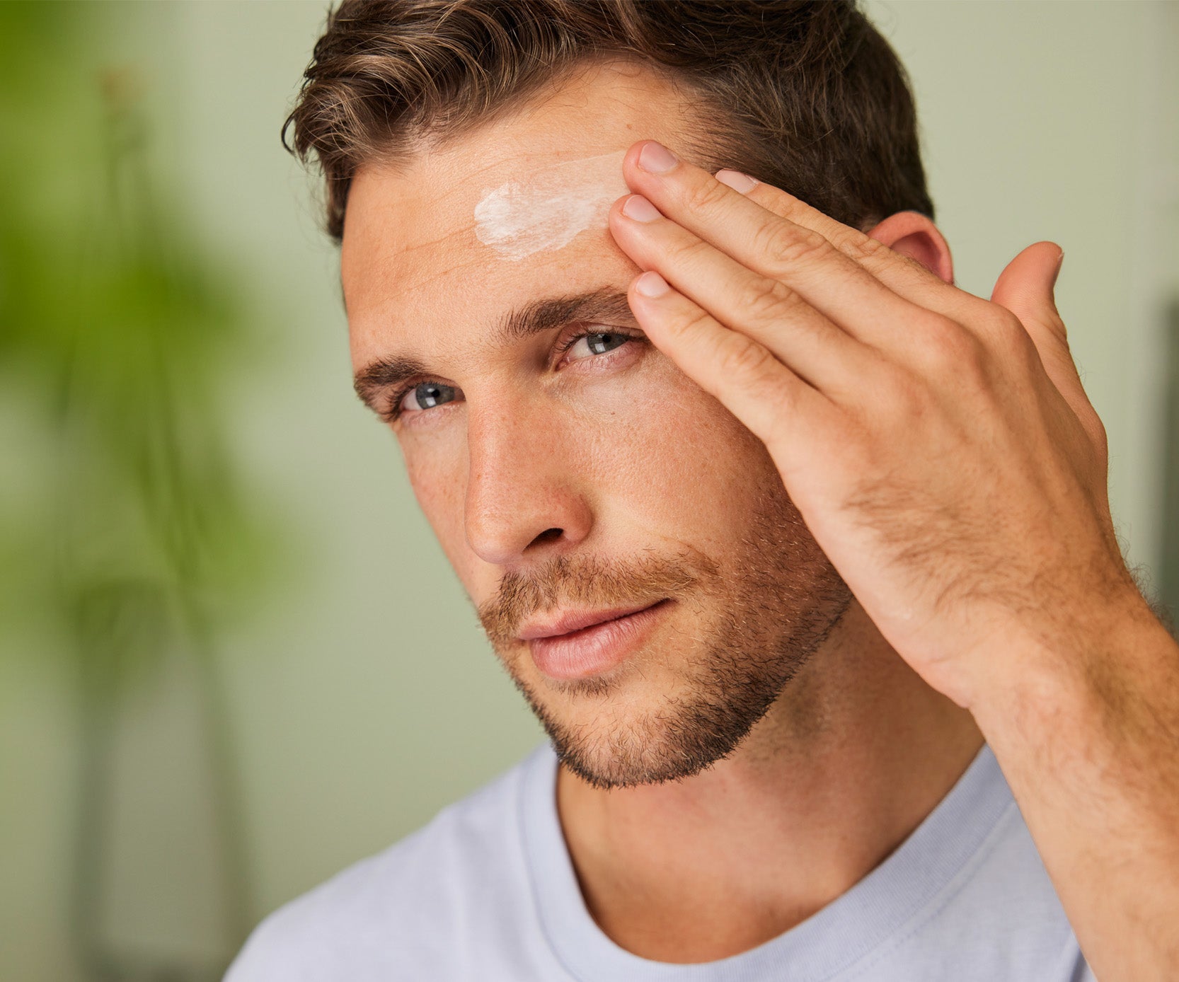 Man applying Weleda Men’s Organic Moisture Cream to his forehead in a bathroom setting.