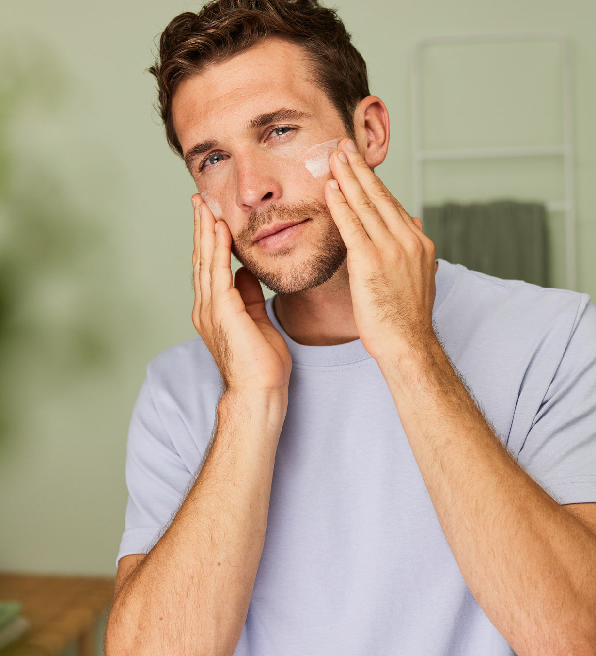 Man massaging Weleda Men’s Moisture Cream natural skincare onto his cheeks with both hands.