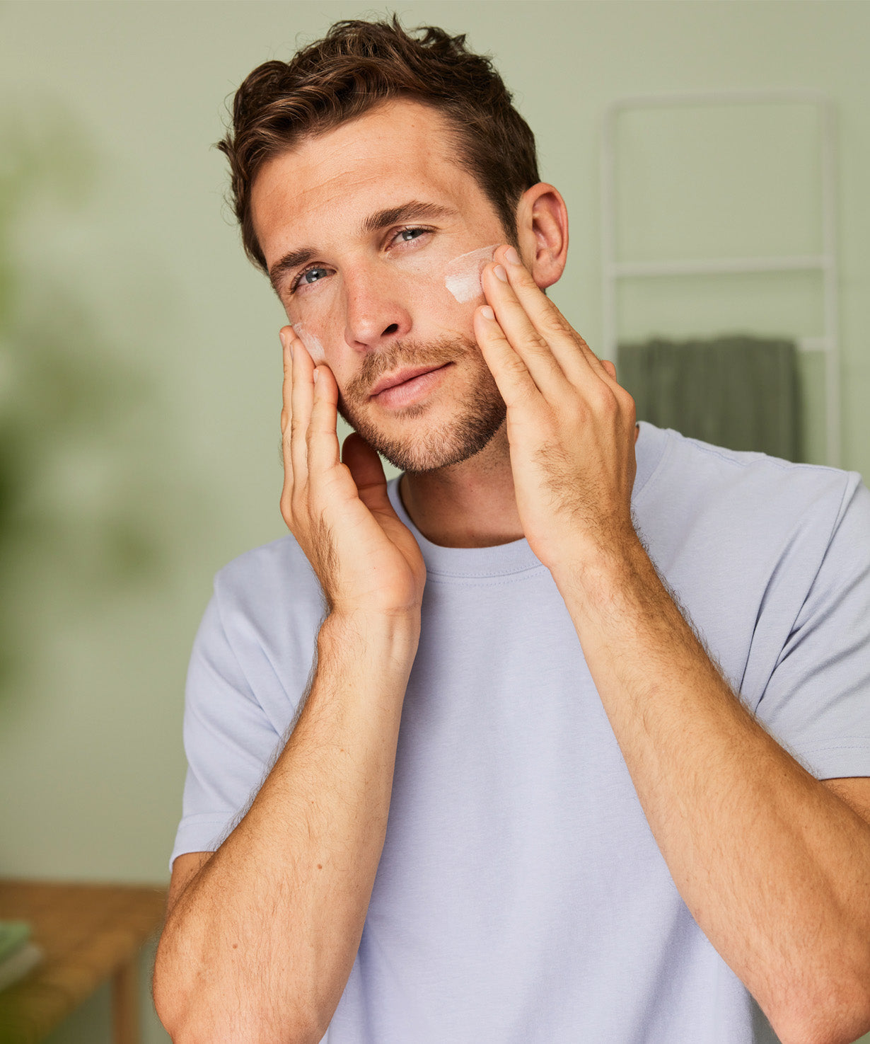 Man massaging Weleda Men’s Moisture Cream natural skincare onto his cheeks with both hands.