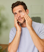 Man massaging Weleda Men’s Moisture Cream natural skincare onto his cheeks with both hands.