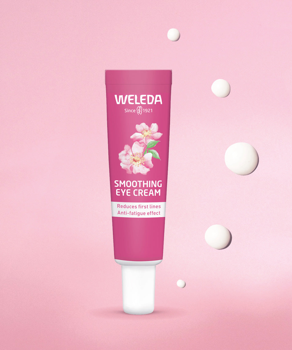 Weleda wild rose and white tea soothing eye cream. Showing a pink tube in front of a pink background with 5 drops of the cream.