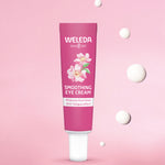Weleda wild rose and white tea soothing eye cream. Showing a pink tube in front of a pink background with 5 drops of the cream.