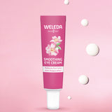 Weleda wild rose and white tea soothing eye cream. Showing a pink tube in front of a pink background with 5 drops of the cream.