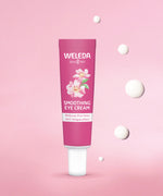 Weleda wild rose and white tea soothing eye cream. Showing a pink tube in front of a pink background with 5 drops of the cream.