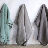 3 Wild and Stone organic cotton hand towels hung up in a line on a white marble background