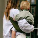 A mother carrying a toddler in the army green Wildride carrier showing the size of the seat and back detail when in use. 
