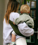 A mother carrying a toddler in the army green Wildride carrier showing the size of the seat and back detail when in use. 