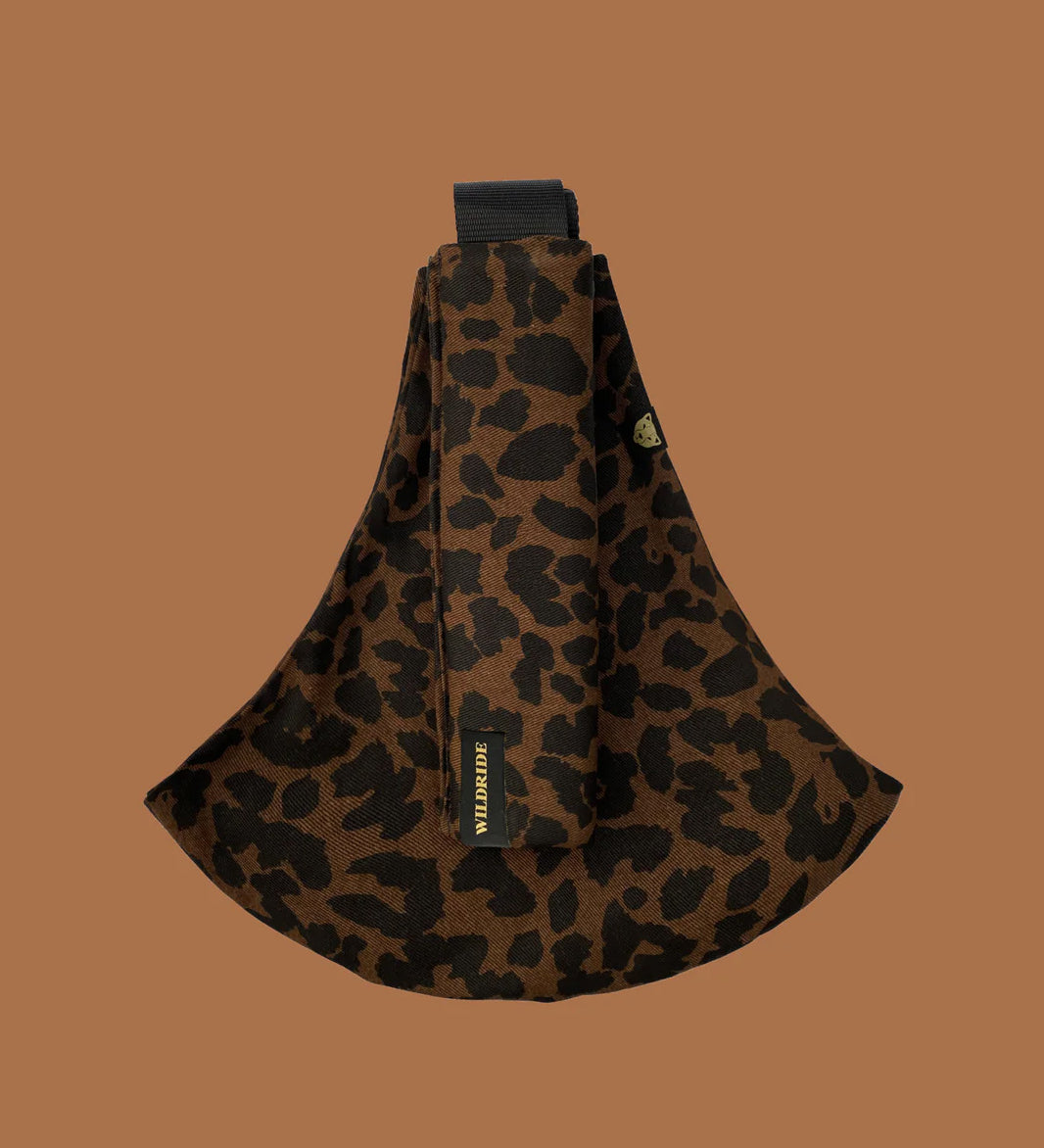 Wildride toddler carrier in brown leopard. A 100% cotton seat stylish hip carrier for babies showing the strap folded over the carrier seat.
