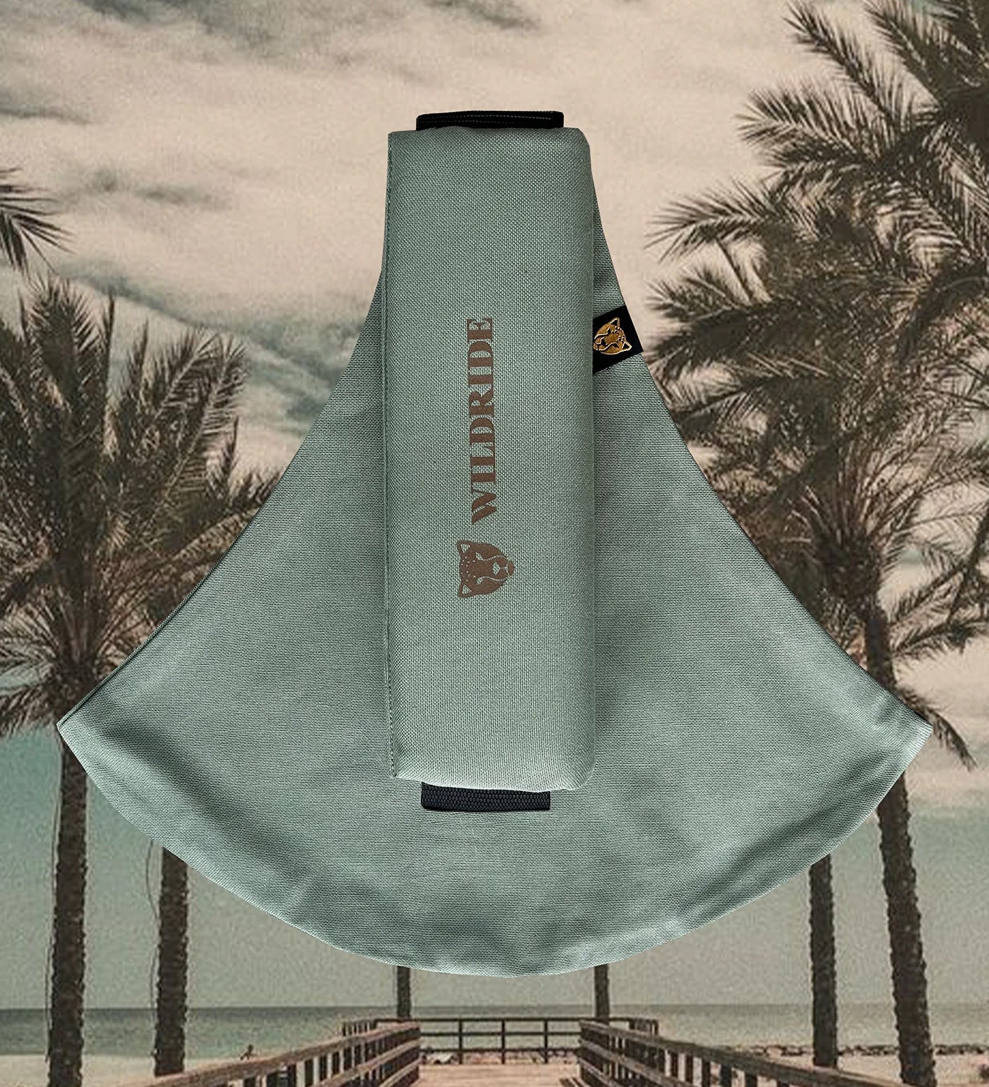 The Wildride fern green toddler carrier, on a background of palm trees