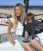 A woman leaning against a yacht, carrying her baby in the stylish Wildride hip sling carrier in grey leopard print 