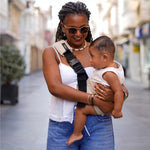 A woman carrying her baby through the city streets with the Wildride Sand Linen ergonomic baby and toddler carrier sling. 