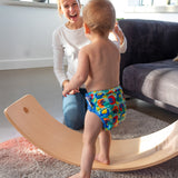 Toddler practising balance on the Babipur edition Wobbel Original beech board with no felt while a parent watches.