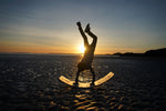Child performing a handstand on the Babipur edition Wobbel Original beech balance board during sunset at the beach.