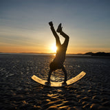Child performing a handstand on the Babipur edition Wobbel Original beech balance board during sunset at the beach.