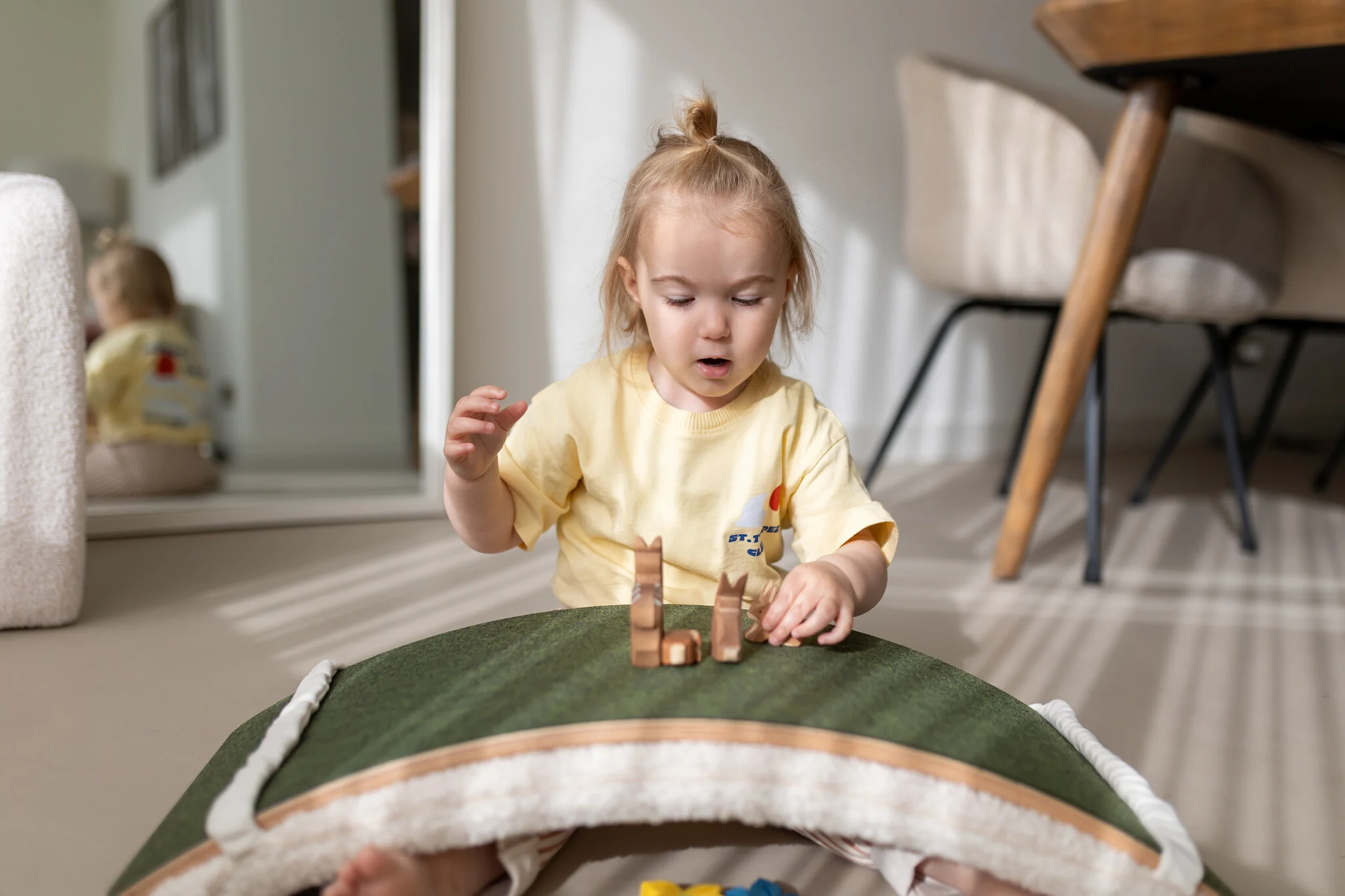 A little girl playing with a Wobbel board with the felt side up, using it as a green bridge for toy animal figures and imaginative play.