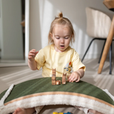 A little girl playing with a Wobbel board with the felt side up, using it as a green bridge for toy animal figures and imaginative play.