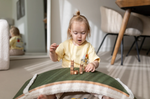 A little girl playing with a Wobbel board with the felt side up, using it as a green bridge for toy animal figures and imaginative play.
