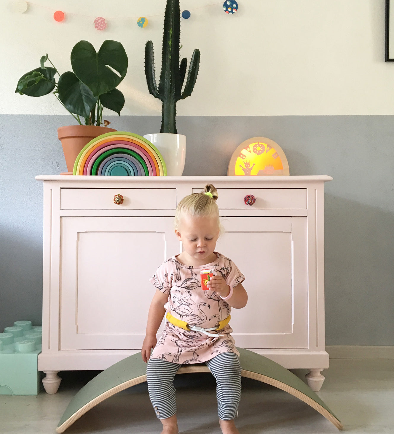 Child sitting on a Wobbel Original beech balance board with wool felt backing in a playroom setting.