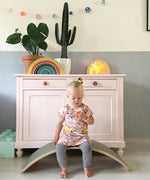 Child sitting on a Wobbel Original beech balance board with wool felt backing in a playroom setting.