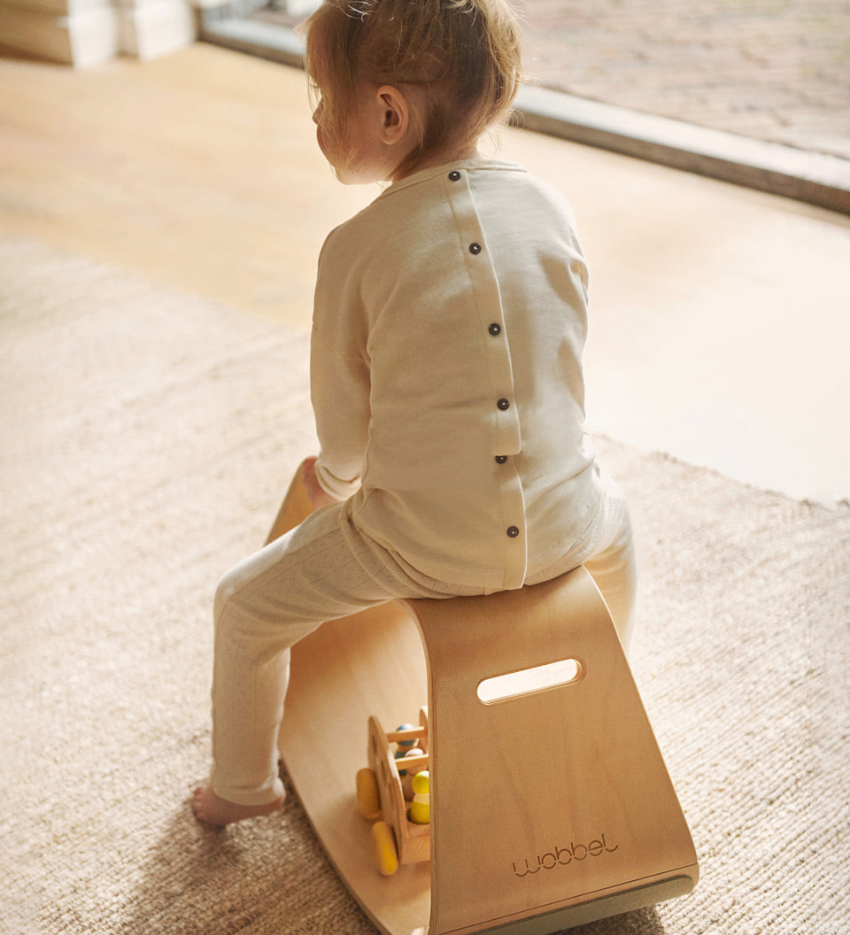 Close up of a young child sat on a plastic-free Wobbel balance box on a grey carpet