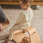 Young girl sat on a Wobbel wooden Up balance box on a grey carpet