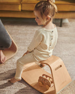 Young girl sat on a Wobbel wooden Up balance box on a grey carpet