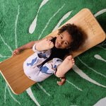 Child laying on a Wobbel Bamboo balance board on a green leaf carpet
