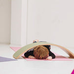 Child crawling underneath a Wobbel Beech Wood balance Board on a yoga mat