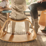 Close up of 3 child sat at a table on a Wobbel curved wooden Up balance box on a grey carpet