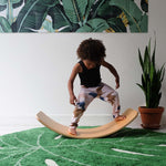 Child balancing on a Wobbel Original Bamboo balance board in a white and green room