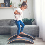 Girl walking on two upturned Wobbel Pro Felt balance boards in front of a grey sofa
