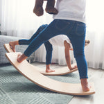 Two children balancing on Wobbel Starter balance boards with felt on a living room carpet