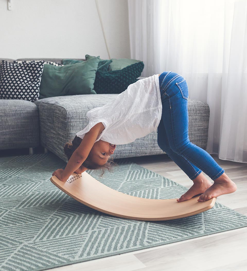 Child playing on a Wobbel Starter Beech Wood wobble board in a white and grey living room