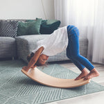 Child playing on a Wobbel Starter Beech Wood wobble board in a white and grey living room